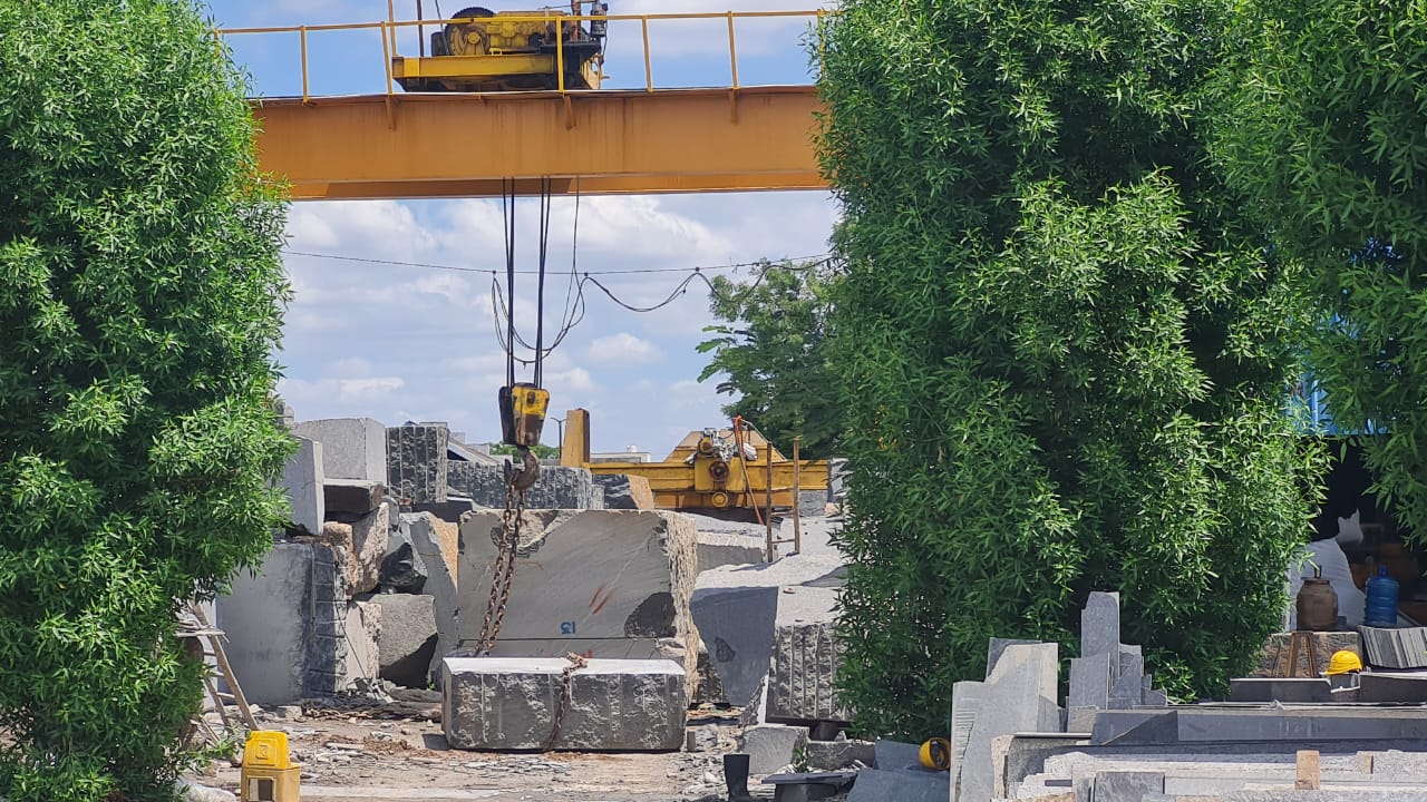 Raw granite block hanging from a gantry crane hook in the block yard